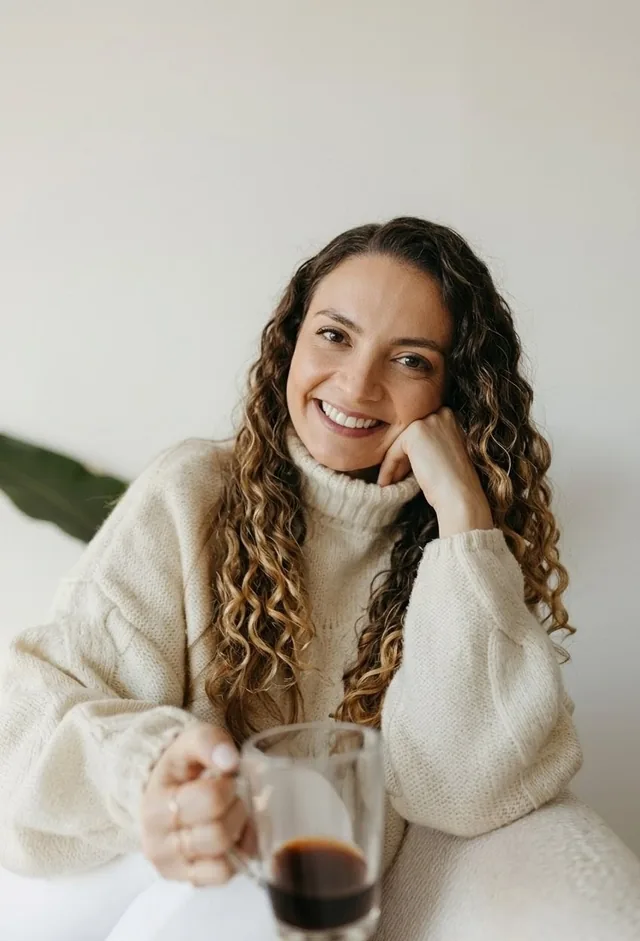 Psicóloga Isabelle Rolim sorrindo, de suéter claro, com uma xícara de café